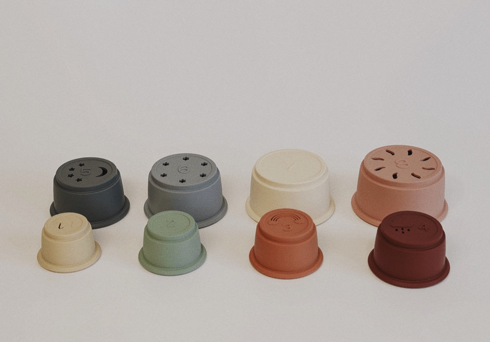 Eight silicone stacking cups in various neutral colors with numbers, enhancing fine motor skills and learning.
