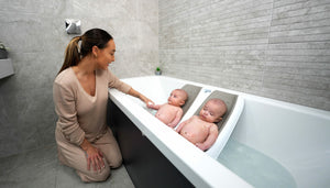 Twin Bath supporting two infants in a bathtub with a woman supervising.
