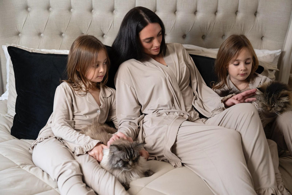 Women and children wearing cinereous luxe lounge sets relaxing on a bed with cats