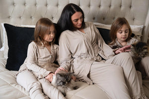 Women and children wearing cinereous luxe lounge sets relaxing on a bed with cats