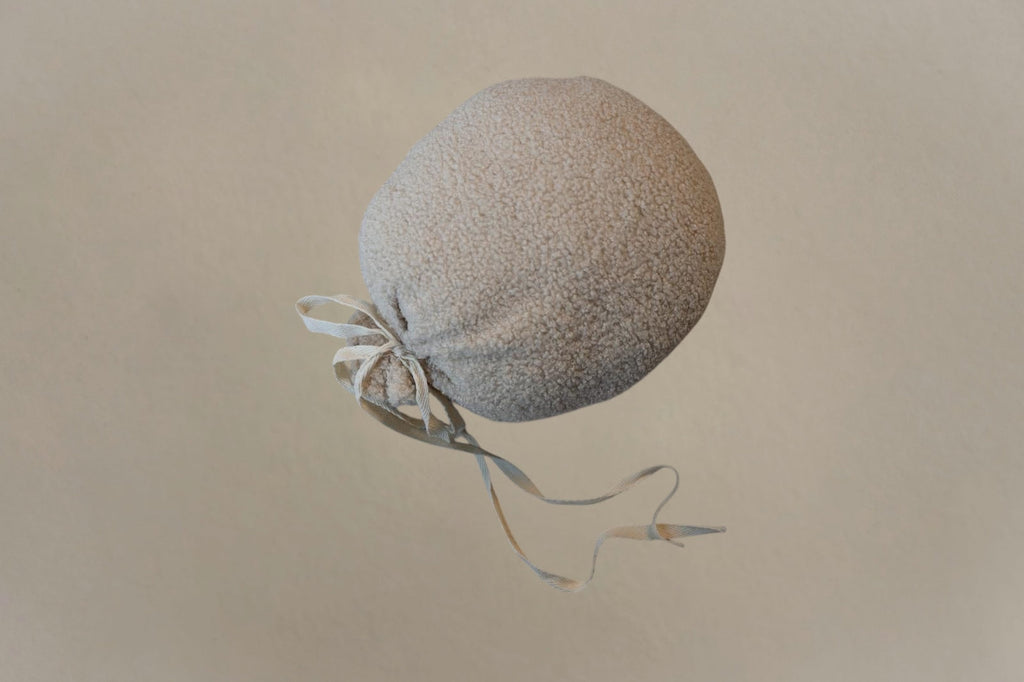 Soft textured biscuit bouclé balloon-shaped nursery cushion with tied ribbon detail