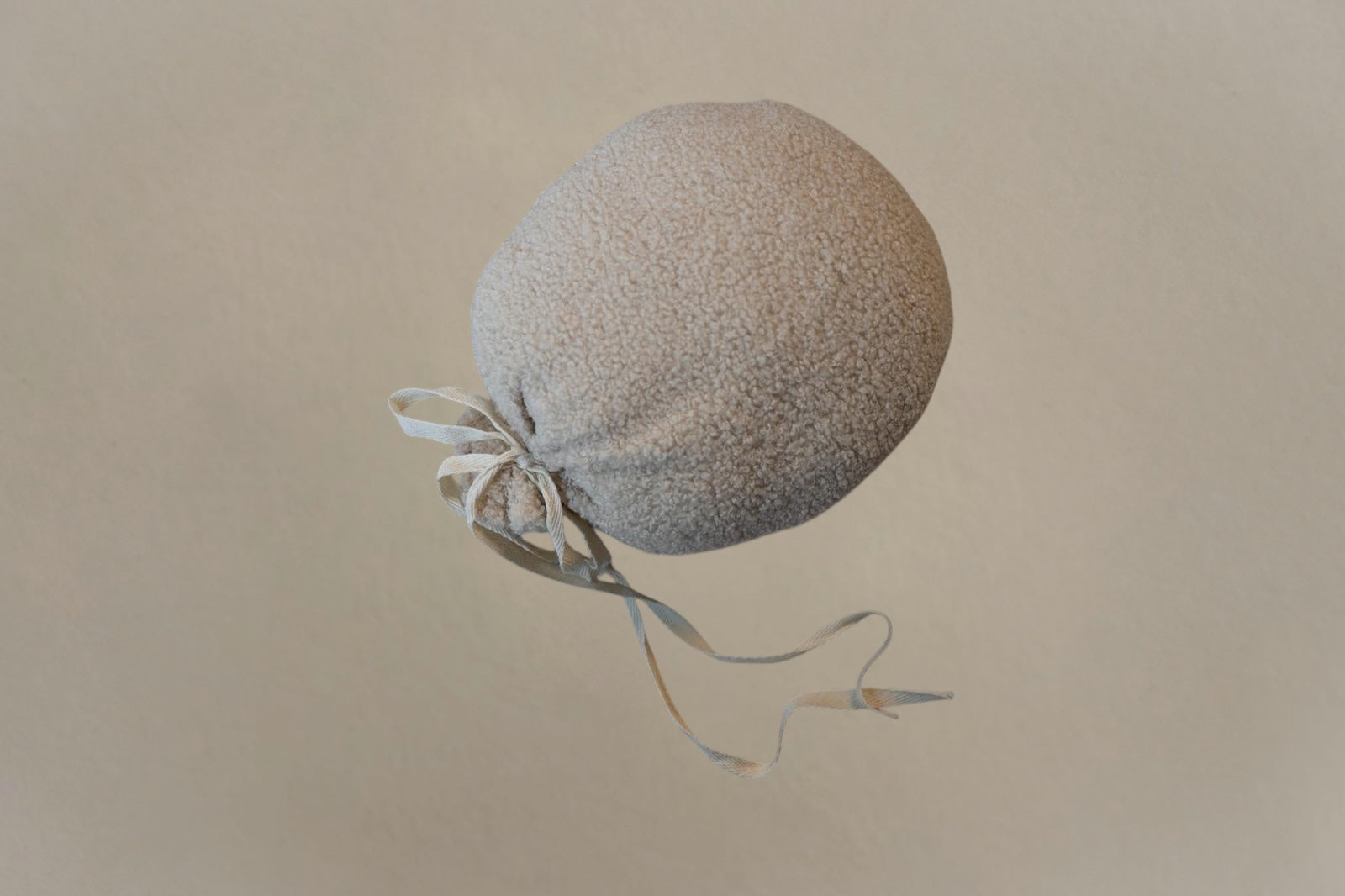 Soft textured biscuit bouclé balloon-shaped nursery cushion with tied ribbon detail