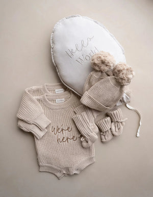 Were Here twin outfit set in biscuit beige with knitted rompers, matching pom-pom hats, booties, and Hello World balloon for newborn twins