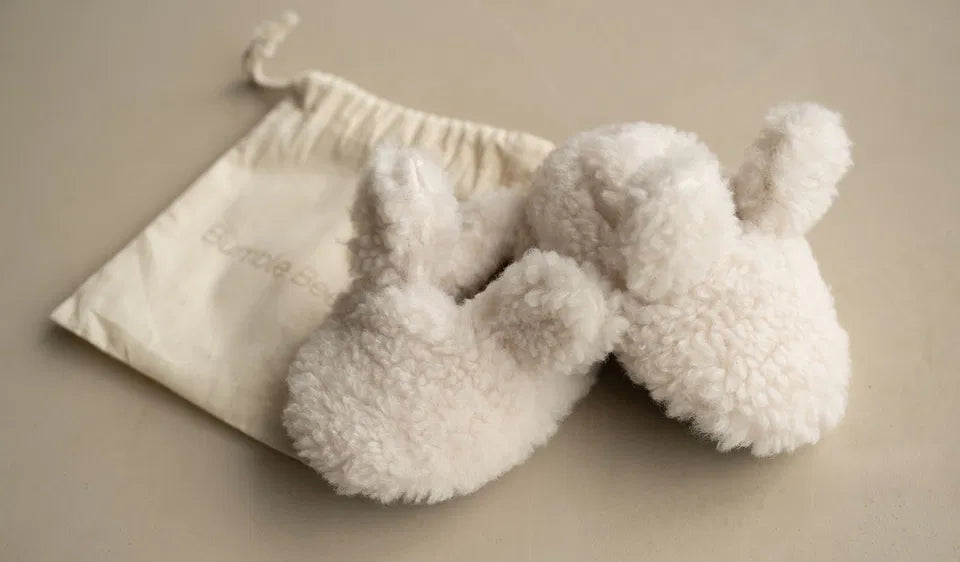 Soft oat-colored Bouclé Bunny Booties for newborns with cotton ties and soft soles, displayed with a cotton drawstring bag.