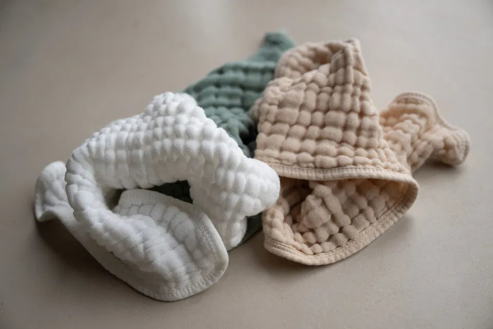 The Cocoon Baby Bath Covers pack of 2 in white, sage green, and linen beige soft muslin fabric for baby bath comfort