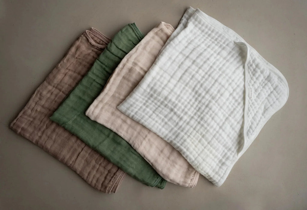 Set of four hooded muslin towels in white, sage green, latte, and beige colors, soft and breathable for babies.