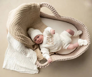 Newborn baby in milk white Hello World Outfit Set with knitted jumper, hat, jam pants, and booties in a basket