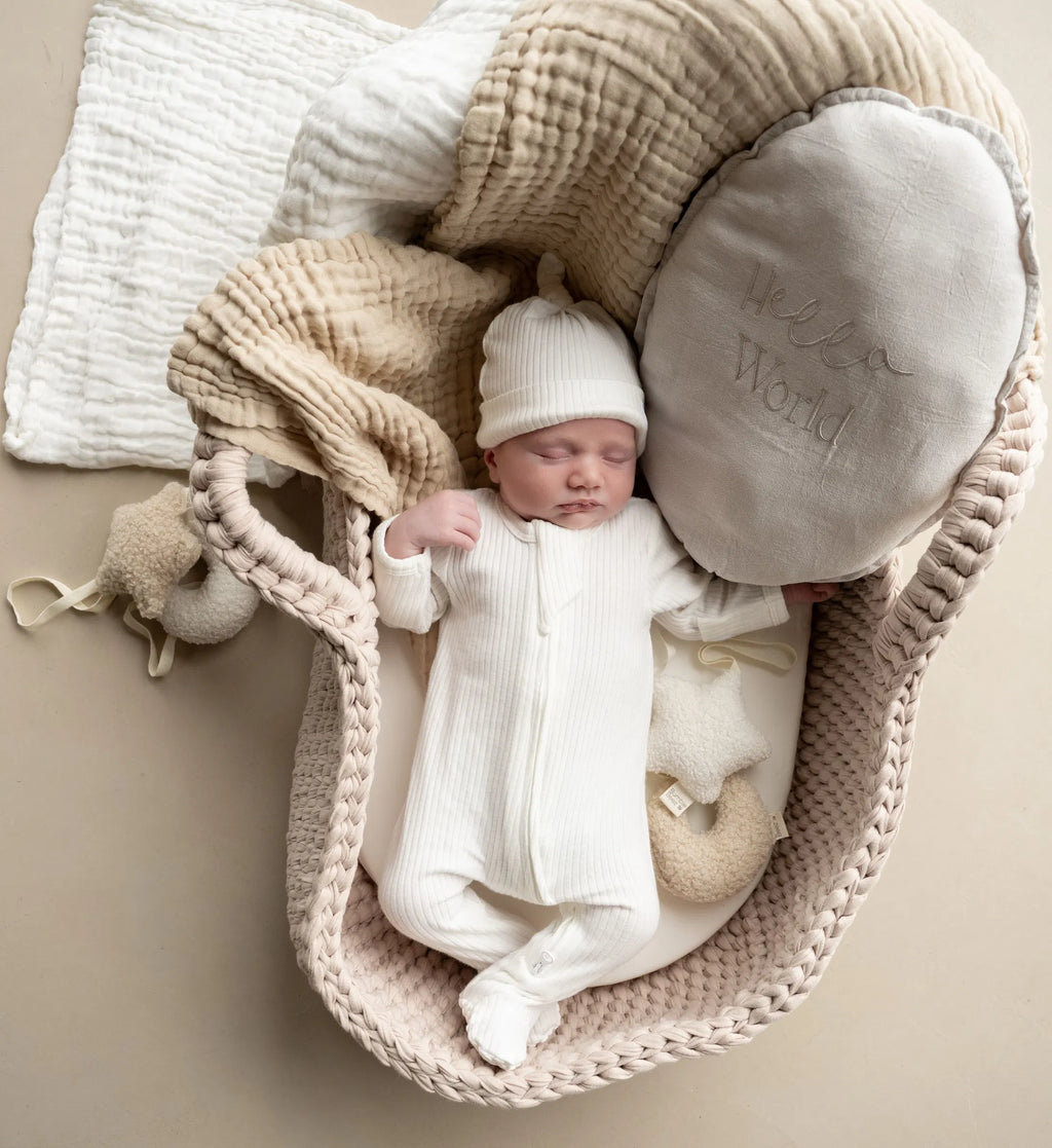 Newborn baby in white The Ribbed Set hat edition organic cotton outfit lying in cozy basket with soft blankets and pillows