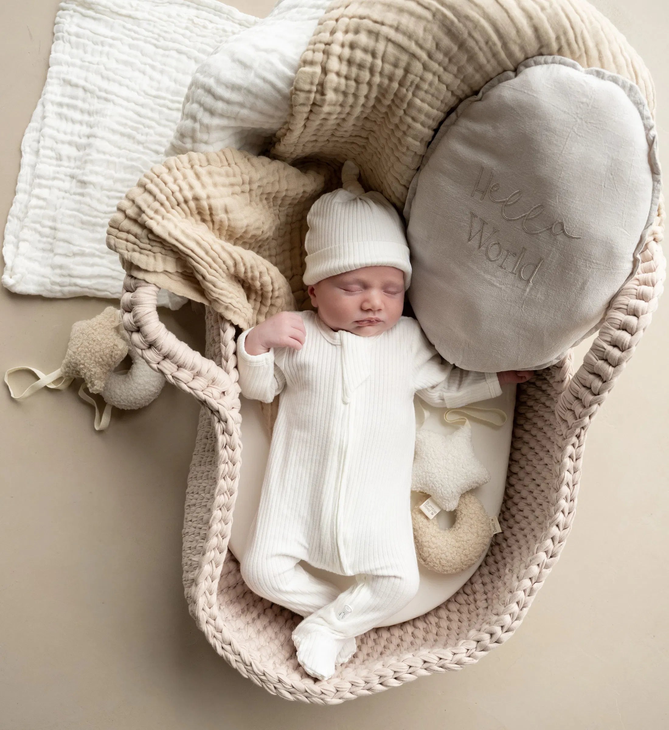 Newborn baby in white The Ribbed Set hat edition organic cotton outfit lying in cozy basket with soft blankets and pillows