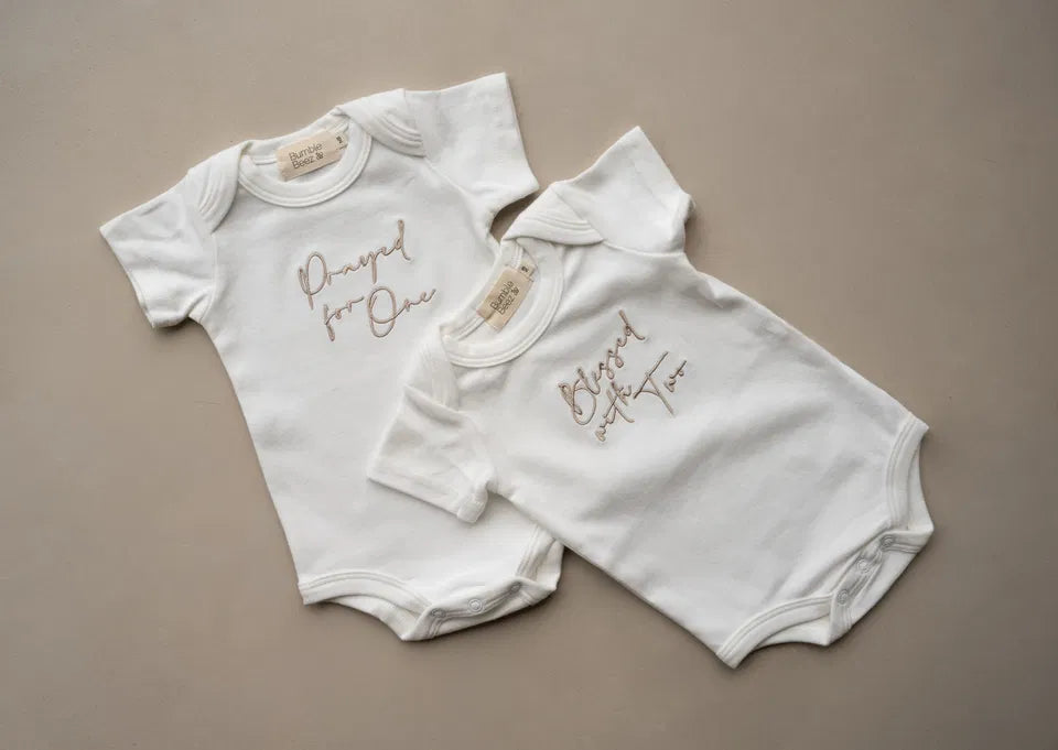 Ivory twin vest set with embroidered “Prayed for One” and “Blessed with Two” text in champagne thread, soft cotton blend baby bodysuits.