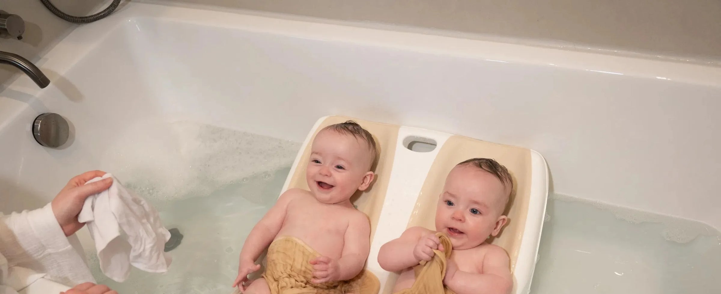 Two babies in a bathtub with one holding a white Cloud Soft Wash Cloths baby washcloth
